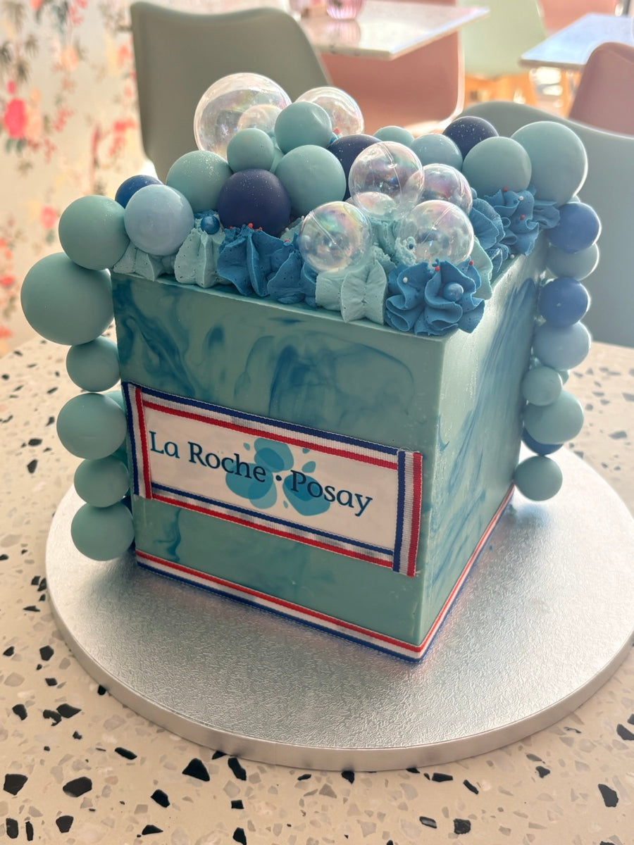 Une création carrée dans les tons bleus, avec son inscription La Roche-Posay et une couronne de sphères pastel et irisées.