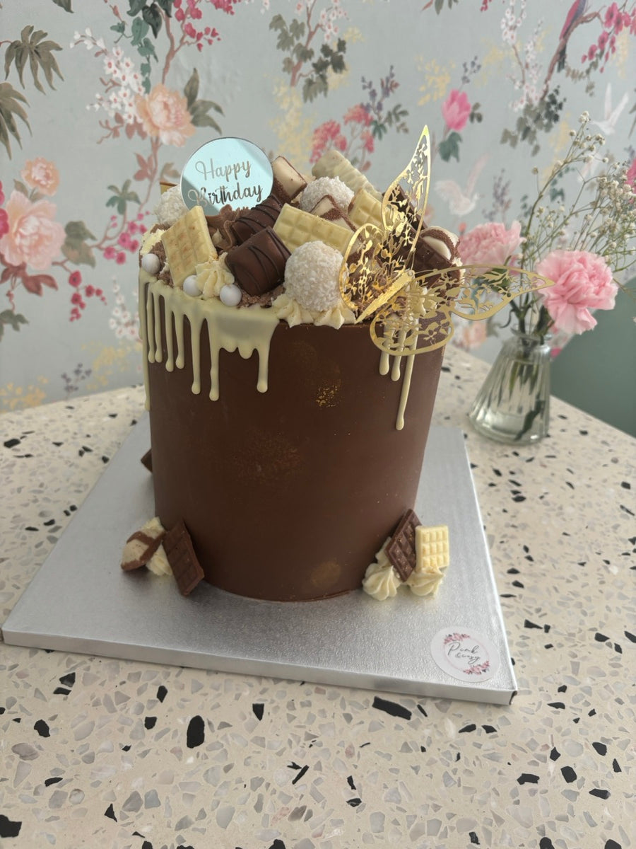 Un layer cake habillé de chocolat, avec des coulures claires, des morceaux de gourmandises et des papillons dorés.