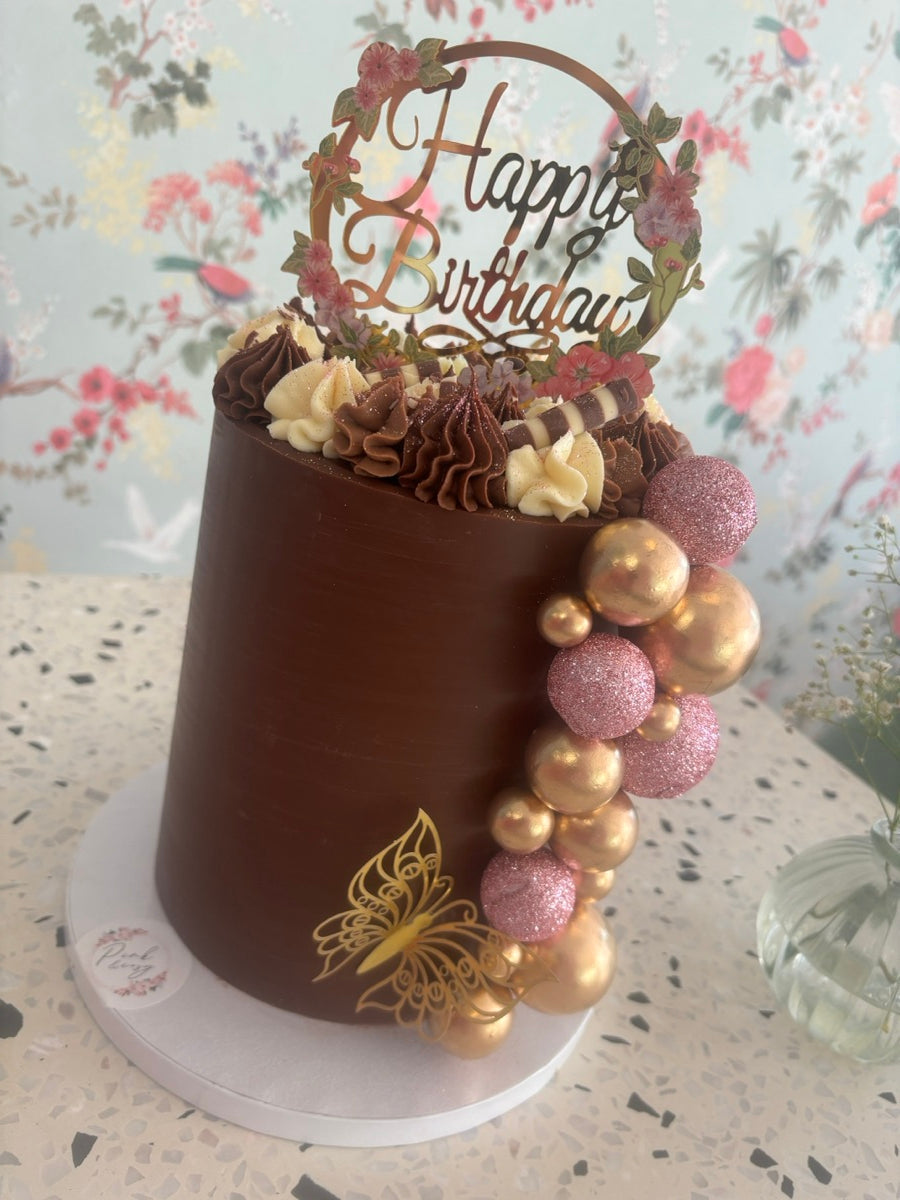 Un gâteau chocolat au décor élégant : des pochages contrastés, une cascade de boules roses et dorées, et des papillons.