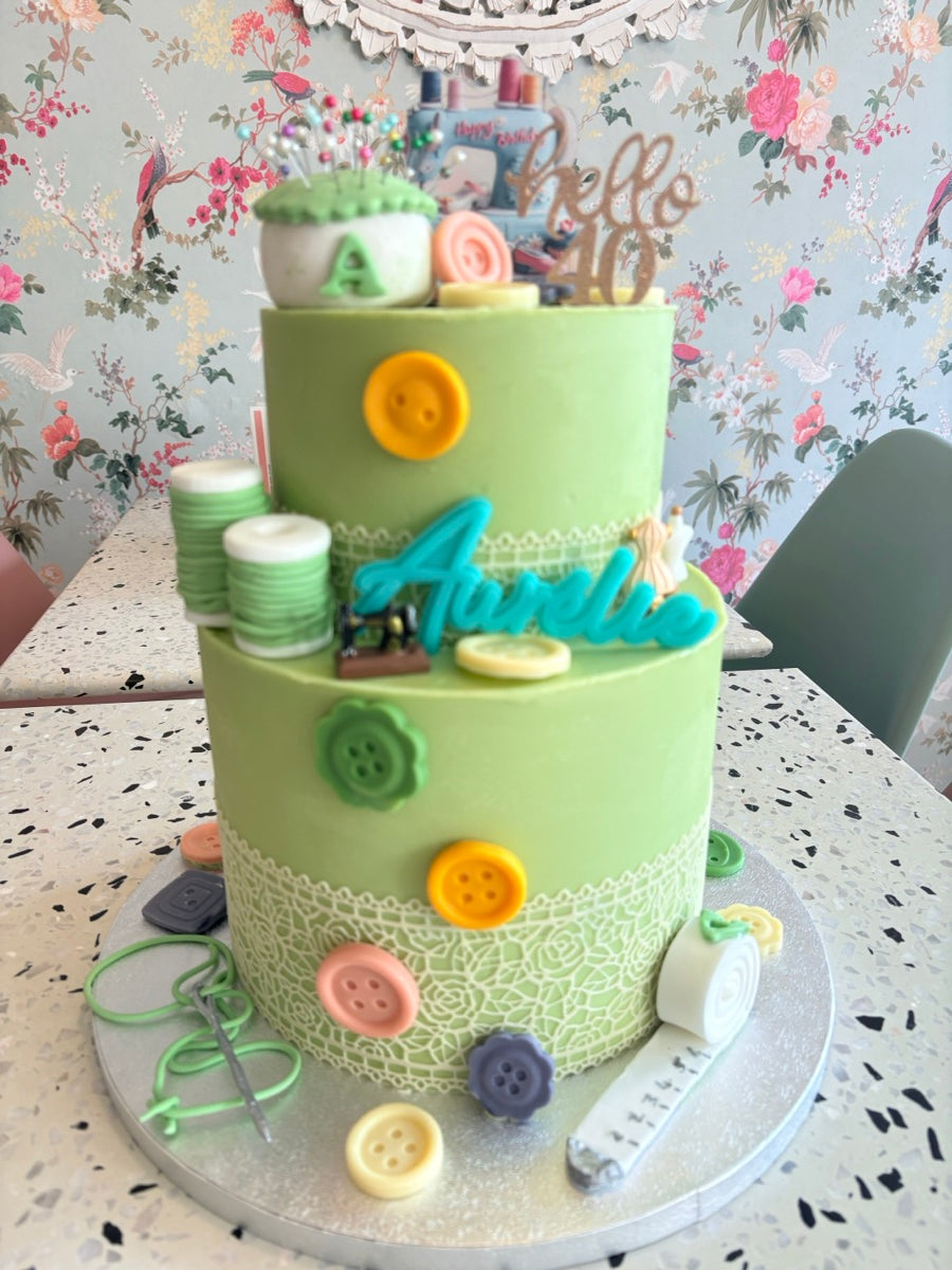 Deux étages vert tendre, des boutons multicolores, des bobines et des détails de dentelle : un gâteau inspiré de la couture.