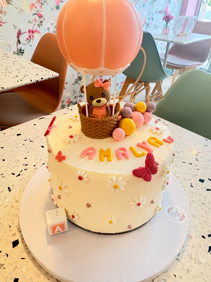 Un petit ourson dans sa nacelle, une montgolfière pêche et un gâteau ivoire fleuri : une création tout en douceur.