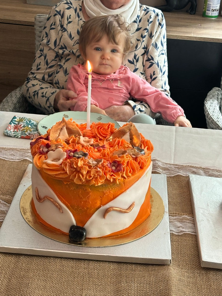 Un gâteau en forme de tête de renard, avec un museau blanc, de grandes oreilles et une couronne de pochages orangés.