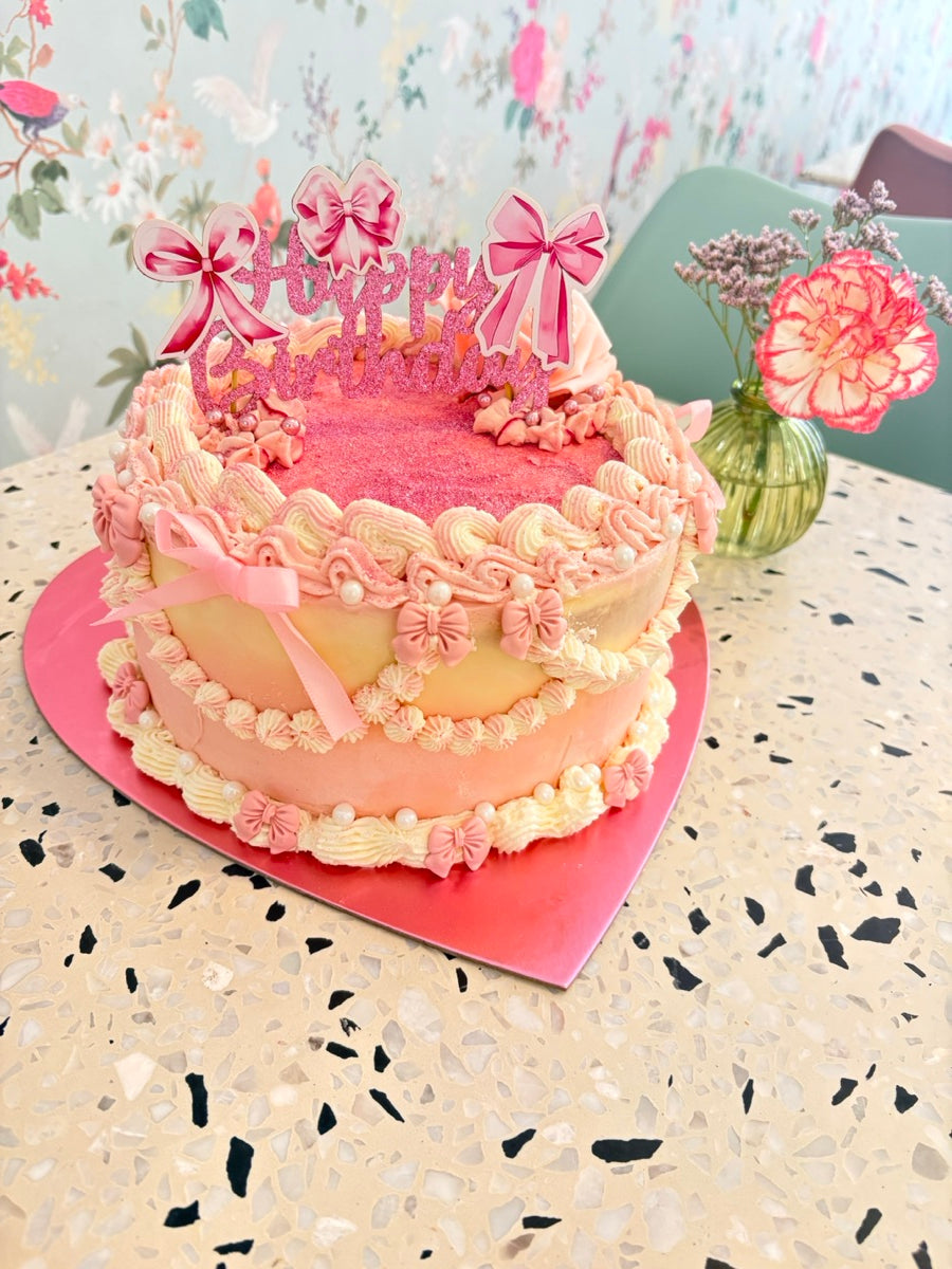 Un décor vintage rose et ivoire : des guirlandes de crème, de petites perles, des nœuds et une touche scintillante.