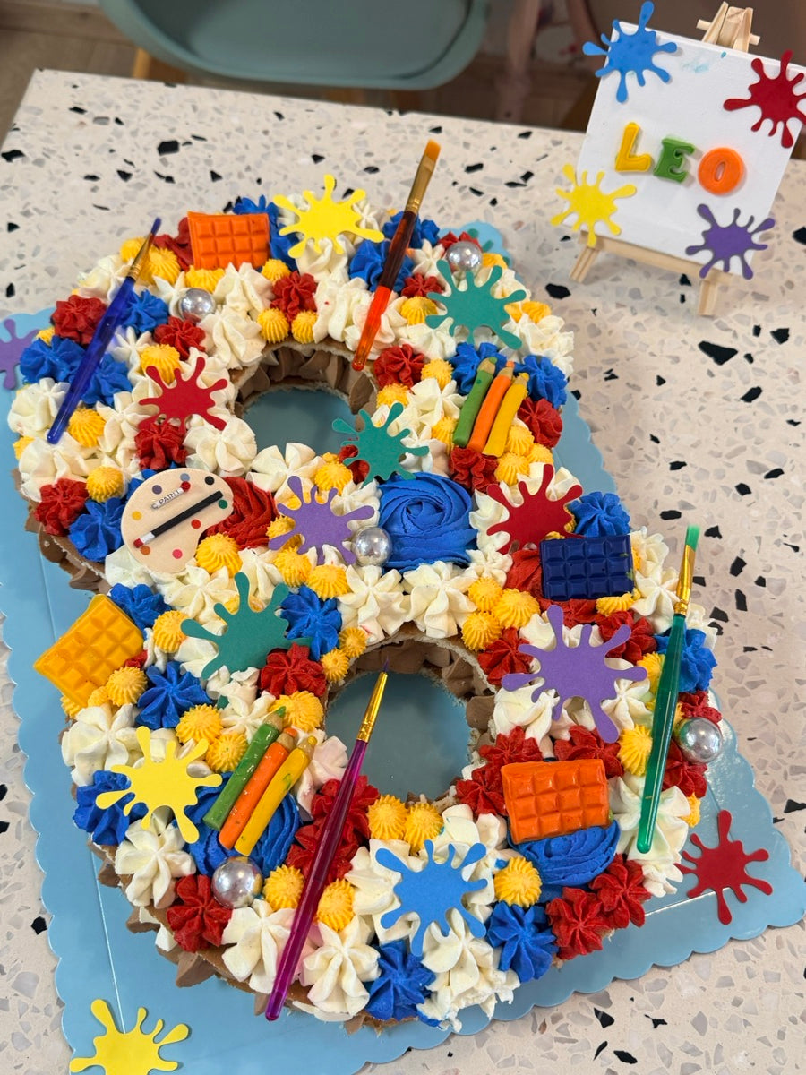 Un chiffre 8 multicolore parsemé de palettes, crayons, touches de peinture et briques décoratives pour les petits créatifs.